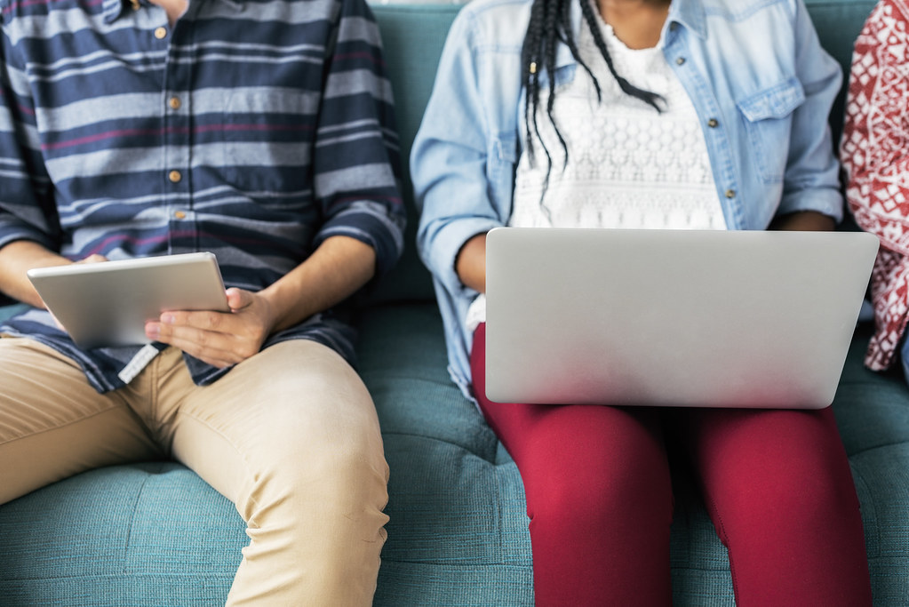 Two people on a couch using a tablet and a laptop